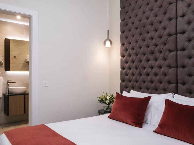 Modern hotel room with large tufted headboard, white bedding, red pillows, and a pendant light.