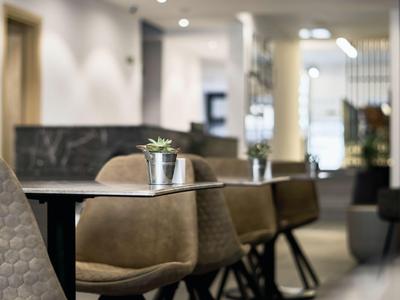 Modern hotel lounge area with padded chairs and small plants on black tables.