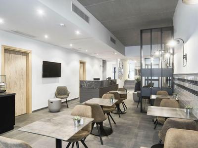 Modern, bright breakfast room with tables, chairs, and a long bench along the wall.