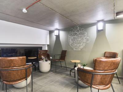 Modern waiting area with leather chairs, small tables, and concrete walls in a hotel.