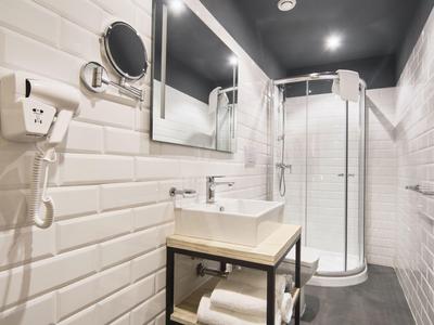 Salle de bain moderne avec cabine de douche, lavabo, miroir et carrelage mural blanc.