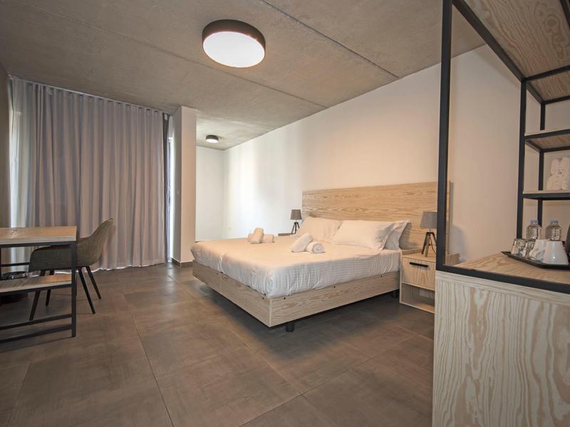 Chambre d'hôtel moderne avec grand lit, bureau et rideaux clairs.