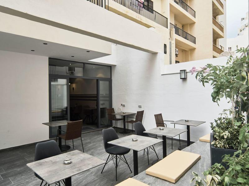 Espace extérieur moderne d'un hôtel avec tables, chaises et banc.