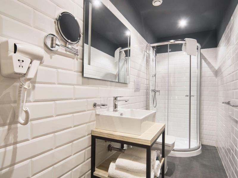 Salle de bain moderne avec cabine de douche, lavabo, miroir et carrelage mural blanc.
