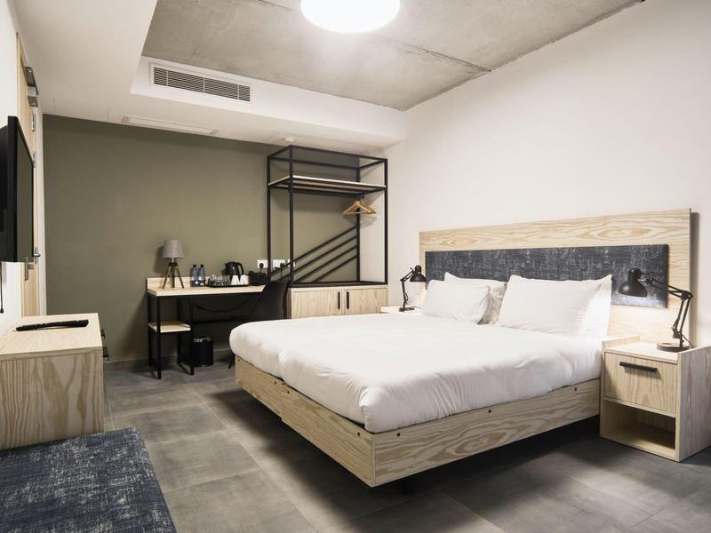 Chambre d'hôtel moderne avec lit double, bureau et télévision à écran plat, aménagement minimaliste.