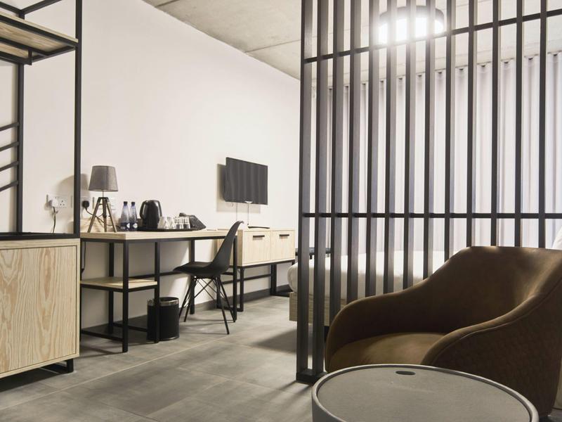 Espace chambre d'hôtel moderne avec coin bureau, télévision et fauteuil confortable.