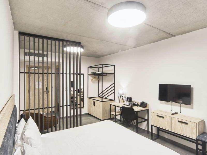 Chambre d'hôtel moderne avec lit blanc, télévision murale et bureau.