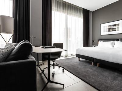 Modern eingerichtetes Hotelzimmer mit großem Bett, Sofa und großem Fenster mit Vorhängen.