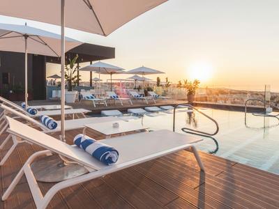 Dakterras met zwembad, ligstoelen en parasols bij zonsondergang in een hotel.