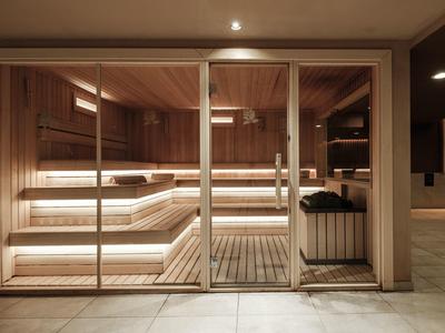 Moderne Holzsauna mit Glasfront, mehrstufigen Bänken und warmem Licht im Spa-Bereich.