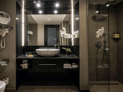 Modernes Badezimmer mit beleuchtetem Spiegel, Waschbecken und Glasdusche in dunklem Design.