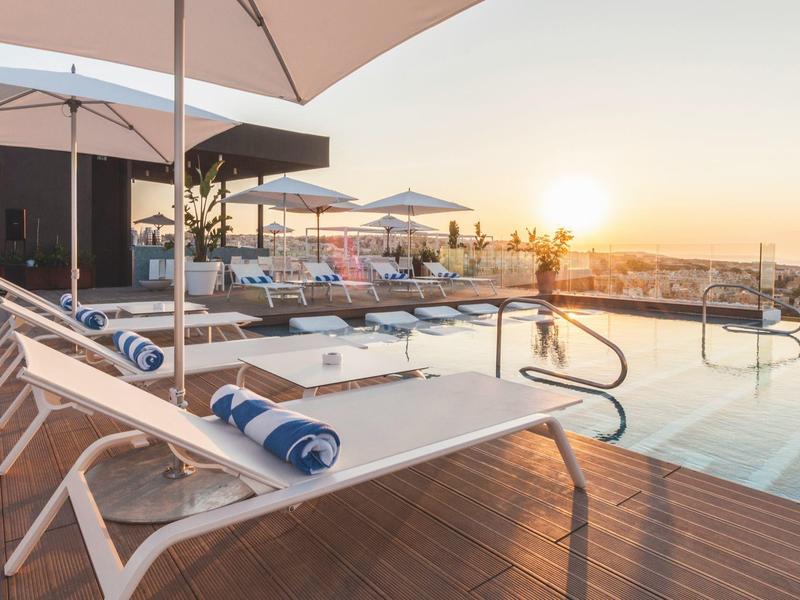 Poolbereich mit Liegestühlen, Handtüchern und einem Sonnenuntergang im Hintergrund.