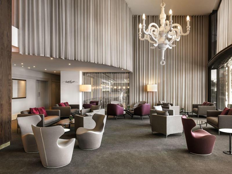 Modernes Hotel-Lounge mit stilvollen Sesseln, großen Fenstern und einem Kronleuchter.