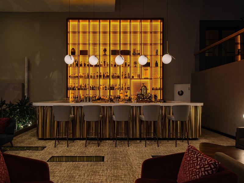 Moderne Bar mit gelber Hintergrundbeleuchtung und fünf Hockern in stilvollem Ambiente