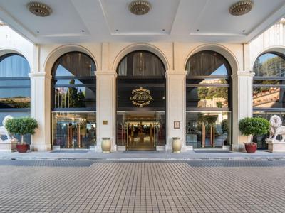 Wejście do hotelu z dużymi oknami w łuk, roślinami i kamiennymi lwami.