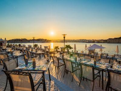 Terrasse mit Tischen und Stühlen am Wasser bei Sonnenuntergang