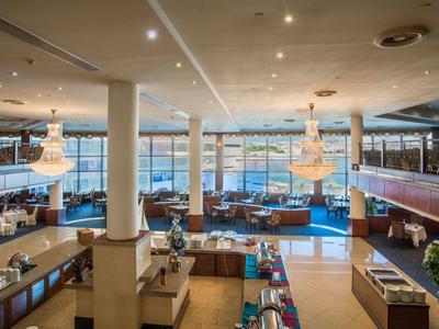 Przestronny hol hotelowy z miejscami do siedzenia, żyrandolami i widokiem na wodę.