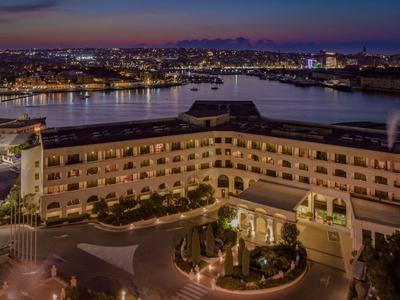 Budynek hotelu z dziedzińcem i basenem nocą z rzeką i światłami miasta w tle