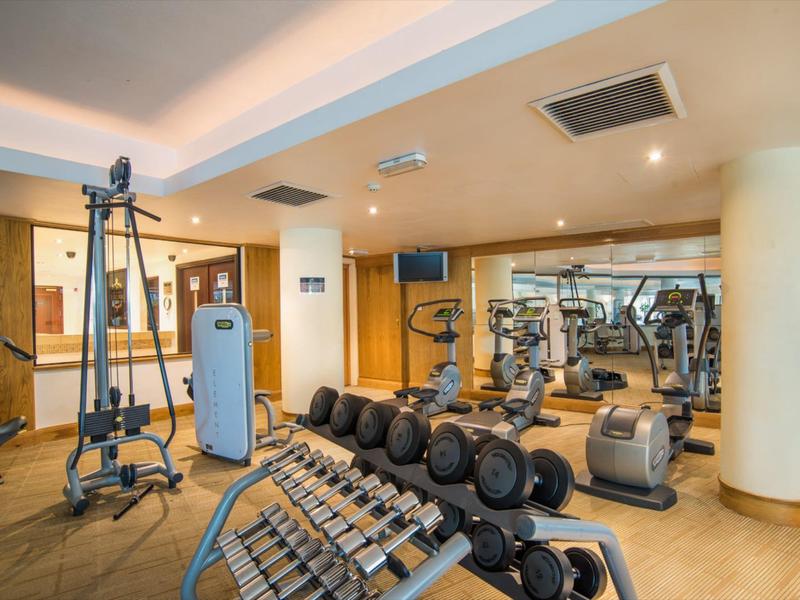 Nowoczesna siłownia z hantlami i różnymi maszynami do ćwiczeń w jasnym wnętrzu.