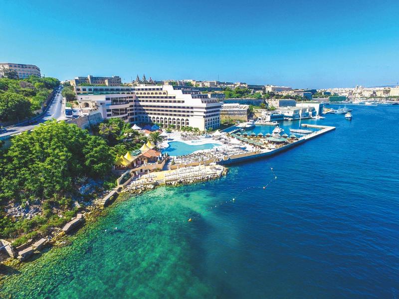 Widok na duży hotel nad morzem z czystą turkusową wodą i bezchmurnym niebem.