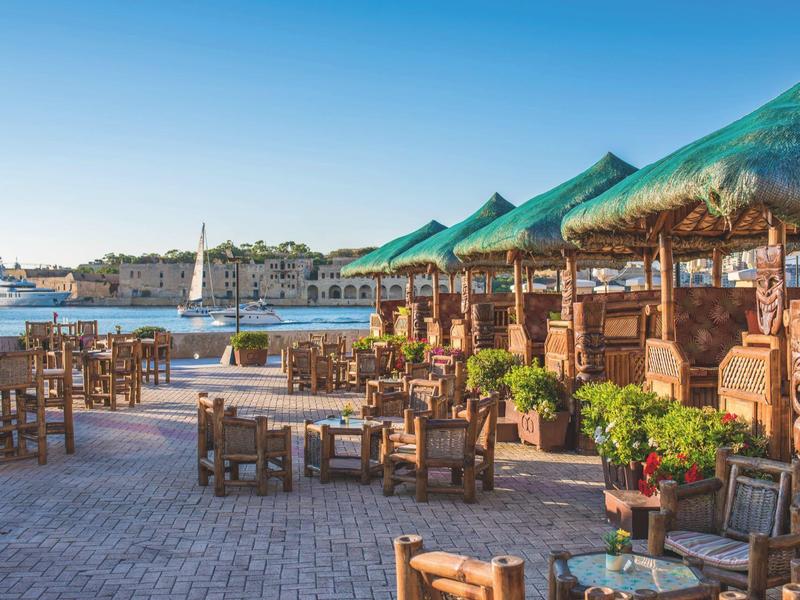 Restauracja na świeżym powietrzu z drewnianymi krzesłami i stołami nad wodą pod słonecznym niebem.