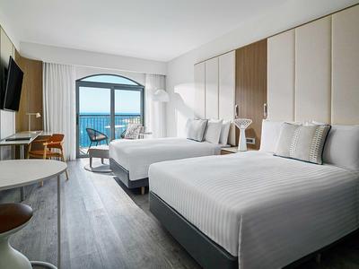 Lichte hotelkamer met twee tweepersoonsbedden, zeezicht en balkon met zitgelegenheid.