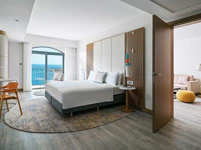 Moderne hotelkamer met twee bedden, groot raam met uitzicht op zee en toegang tot een zithoek.