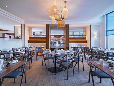 Een modern restaurant met houten stoelen en ronde tafels, versierd met lampen en grote ramen.