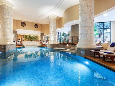 Licht overdekt zwembad met grote zuilen en ligstoelen naast het water