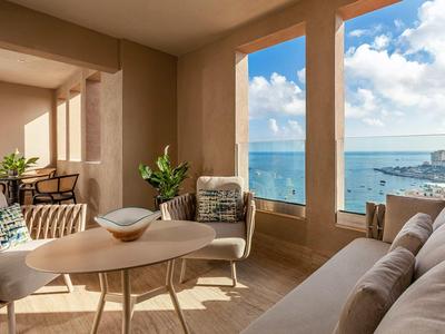 Lichte woonkamer met grote ramen met uitzicht op zee, gezellige meubels en decoratieve planten.