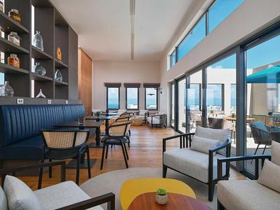 Helles modernes Wohnzimmer mit großen Fenstern, Sitzgruppen, Holzboden und blauen Polstern.