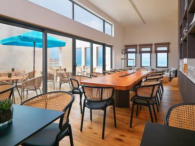 Moderner, heller Essbereich mit Holzboden, großen Fenstern und unterschiedlichen Sitzmöbeln innen und außen.