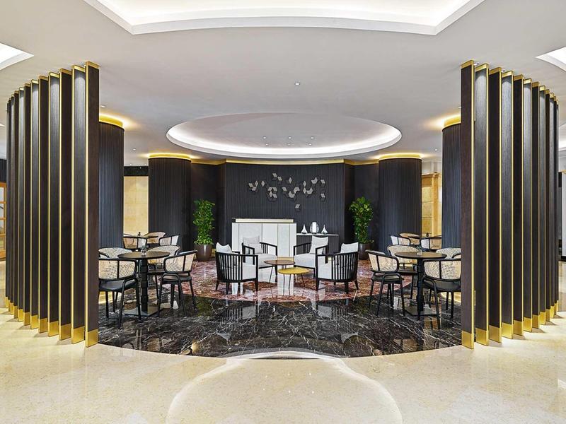 Moderner Lounge-Bereich mit schwarzen Säulen, runden Teppichen und weißen Sesseln auf beigem Boden.