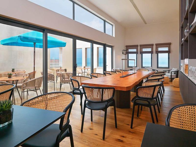 Moderner, heller Essbereich mit Holzboden, großen Fenstern und unterschiedlichen Sitzmöbeln innen und außen.