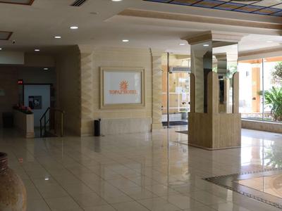 Ampia hall d'hotel con pavimenti in marmo chiaro, colonne e banco ricevimento sullo sfondo.