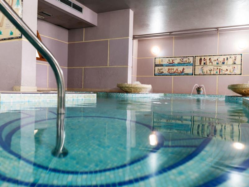 Vnitřní hotelový bazén s odrazy světla a zábradlím v popředí.