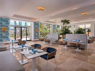Sala colazione luminosa e moderna con grandi finestre, sedie blu e piastrelle di marmo.