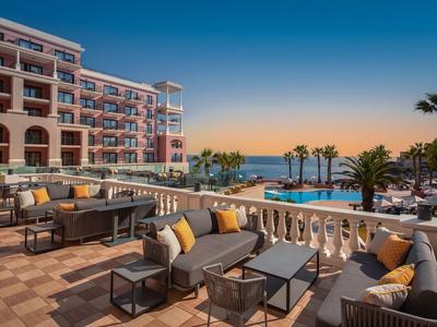 Terrazza dell'hotel con comode sedute, palme e vista sul mare al tramonto