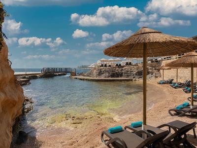 Sonnenschirme und Liegen am felsigen Strand mit klarem Wasser und blauem Himmel.