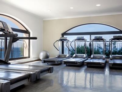 Palestra con diversi tapis roulant davanti a grandi finestre con vista sulla città.