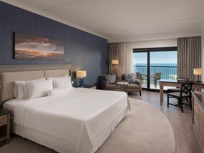 Modernes Hotelzimmer mit großem Bett, Sitzbereich und Meerblick durch großes Fenster.