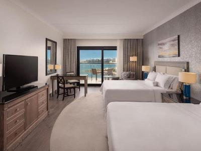 Hotelzimmer mit zwei Betten, Sitzbereich und Blick auf das Meer durch eine Glasfront