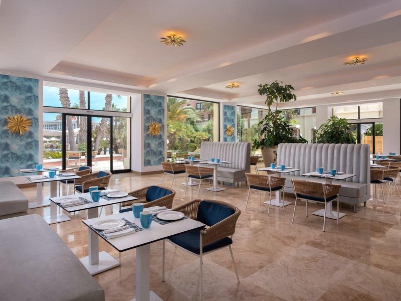 Helle, moderne Hotel-Lounge mit Polstersesseln, Tischen und großen Fenstern mit Außenblick.