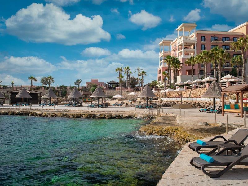Blick auf einen Hotelstrand mit Liegestühlen, Palmen und türkisfarbenem Wasser bei sonnigem Wetter.