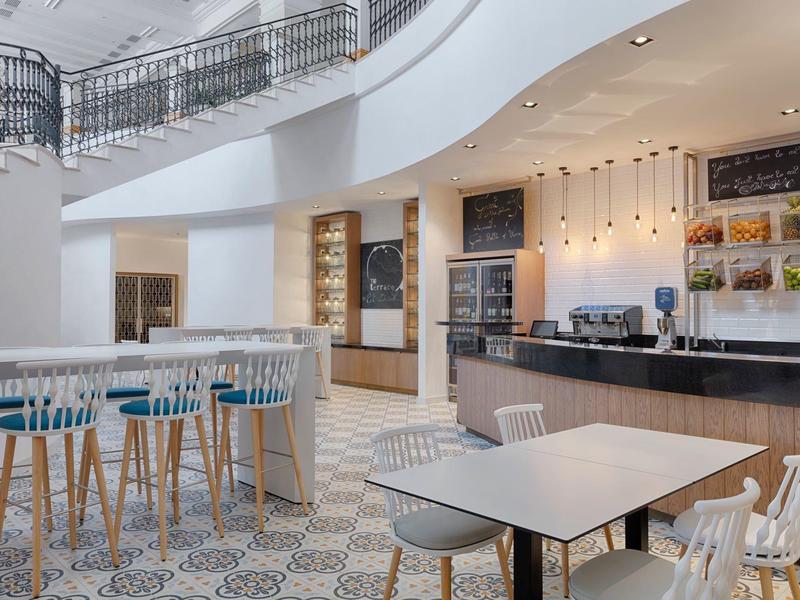 Moderner Frühstücksraum mit Barhockern, weißen Tischen und Stühlen, hell und einladend.