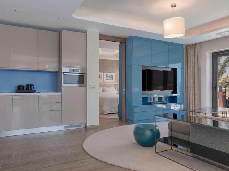 Modern eingerichtetes Wohnzimmer mit Küchenzeile in neutralen Tönen und blauer Akzentwand.