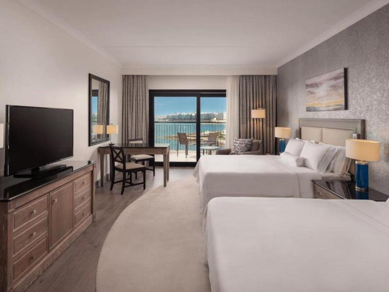 Hotelzimmer mit zwei Betten, Sitzbereich und Blick auf das Meer durch eine Glasfront