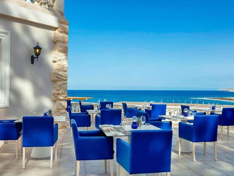 Terrasse mit blauen Stühlen und Tischen mit Blick auf das Meer bei klarem Himmel.