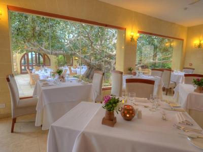 Comedor luminoso con mesas, manteles blancos y vista a un jardín.