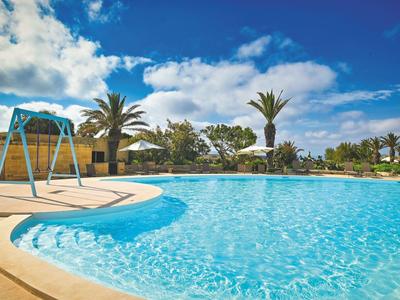 Ein Außenpool mit klar blauem Wasser, umgeben von einer Terrasse und Palmen unter einem blauen Himmel.